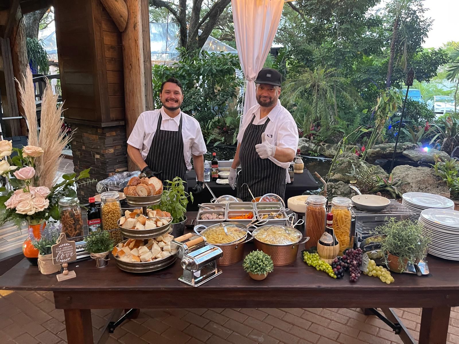 Two chefs at an outdoor pasta station with fresh ingredients